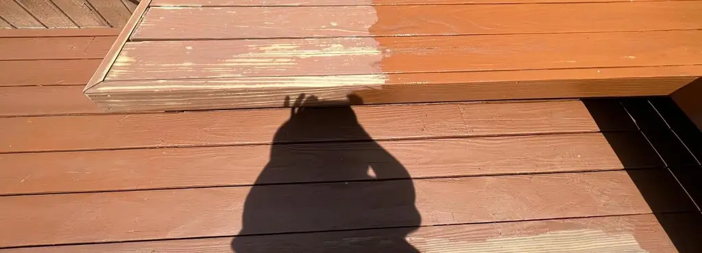 A built-in deck bench half re-stained: weathered grey-tan on the left, fresh cedar red on the right